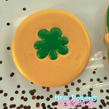 Load image into Gallery viewer, A close-up of a circular sugar cookie designed to look like a gold coin. The cookie is iced with a shimmering, metallic gold royal icing. A small, bright green shamrock is piped in the center, creating a raised, dimensional effect.