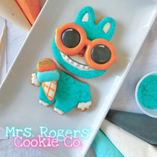 Load image into Gallery viewer, Cookie shaped like a character with sunglasses on a white plate, with &#39;Mrs. Rogers&#39; Cookie Co.&#39; branding.
