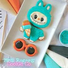 Load image into Gallery viewer, Cookie decorated like a character in a blue costume with orange glasses on a white plate, with &#39;Mrs. Rogers&#39; Cookie Co.
