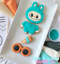 Load image into Gallery viewer, Cookie shaped like a character in a blue outfit with sunglasses on a white plate, branded &#39;Mrs. Rogers&#39; Cookie Co&#39;.

